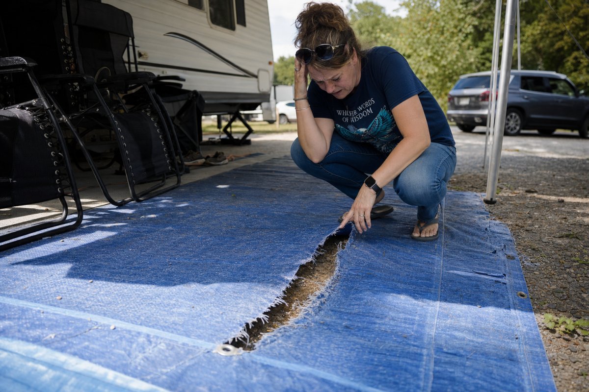 Woman inspecting torn camping mat under RV awning, showing seam separation and damage.