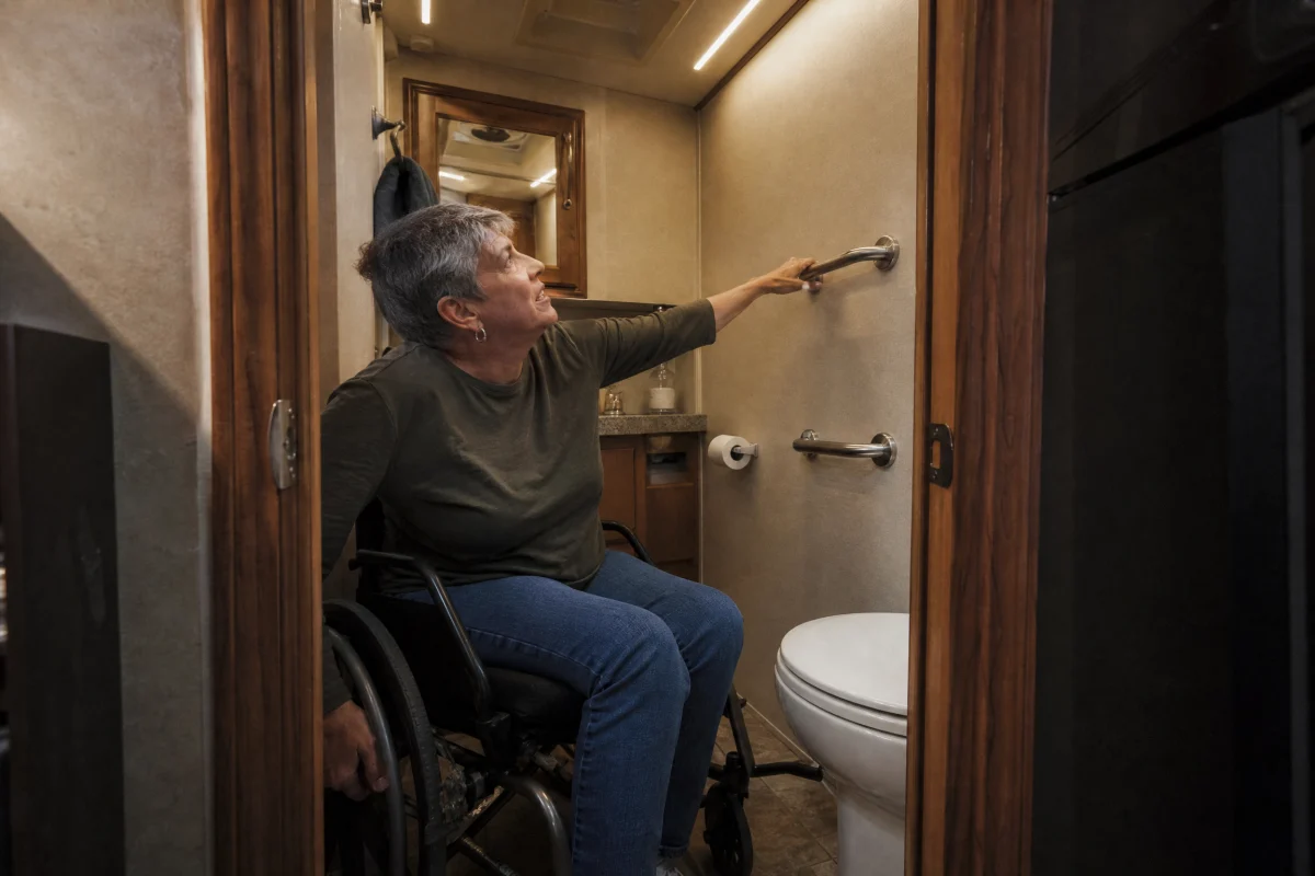Woman in wheelchair reaching toward poorly positioned grab bar in RV bathroom, demonstrating inaccessible rv features.