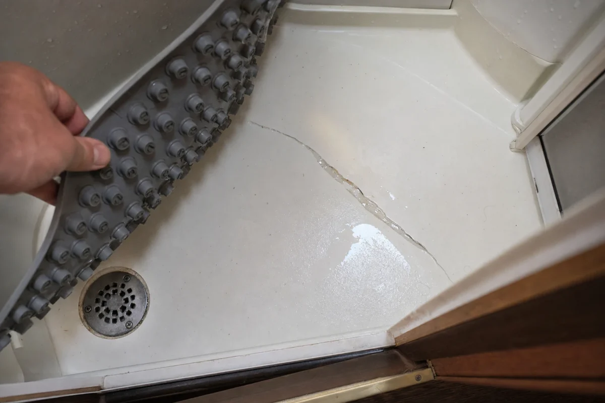 Cracked fiberglass RV shower pan with water pooling in fracture, showing wear from daily use.